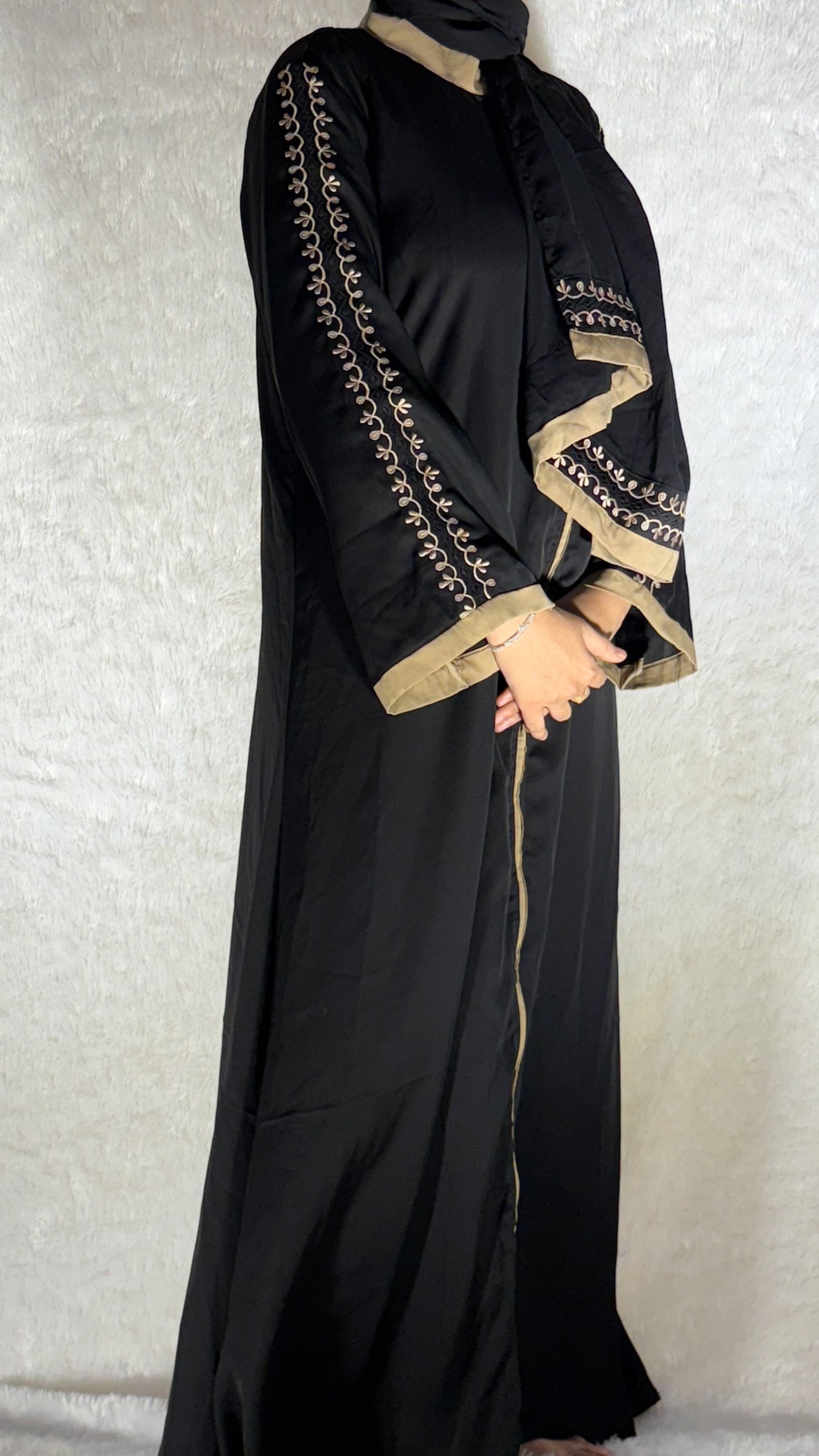 Black abaya with gold embroidery on a neutral background